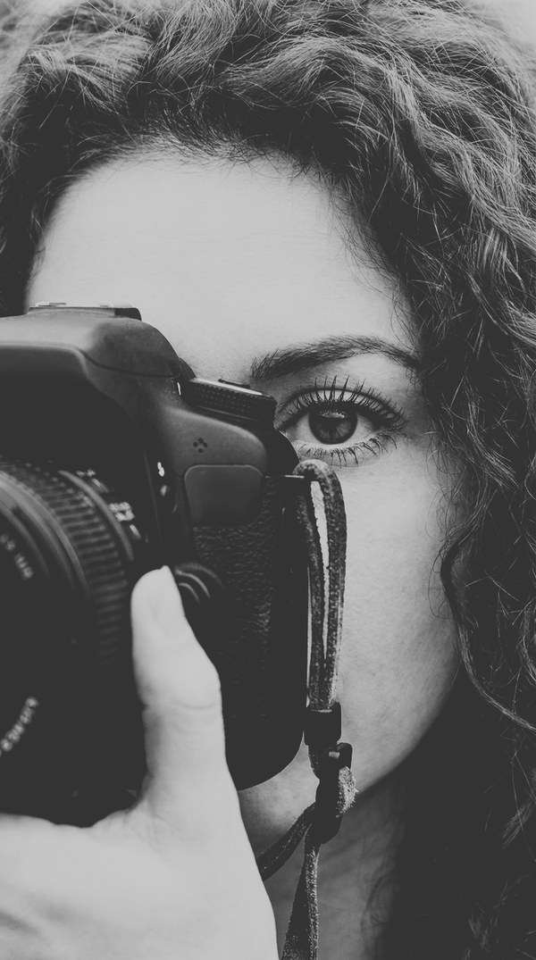 Temporary cover for Through the Shutter: a woman's face behind a camera, in black and white